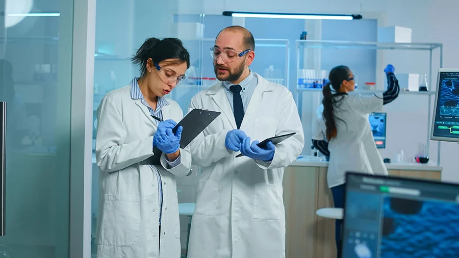 grupo-de-investigadores-medicos-que-discuten-sobre-el-desarrollo-de-vacunas-de-pie-en-un-laboratorio-equipado-apuntando-una-tableta-y-tomando-notas.jpg